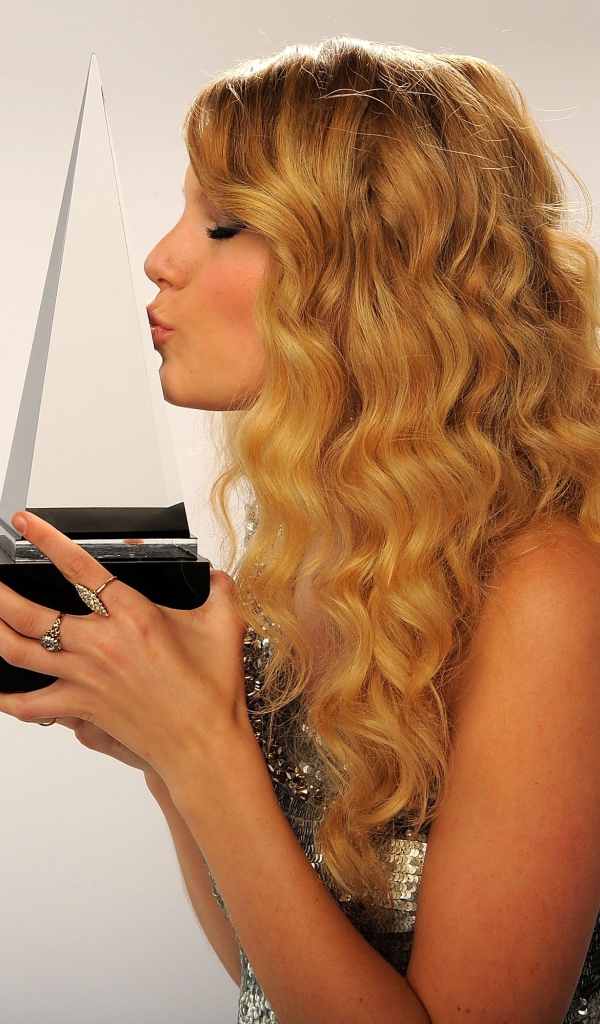 Певица Тейлор Свифт целует награду на сером фоне