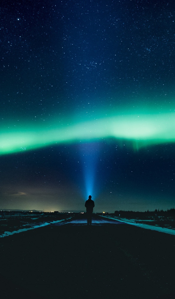 Человек идет по дороге ночью на фоне северного сияния
