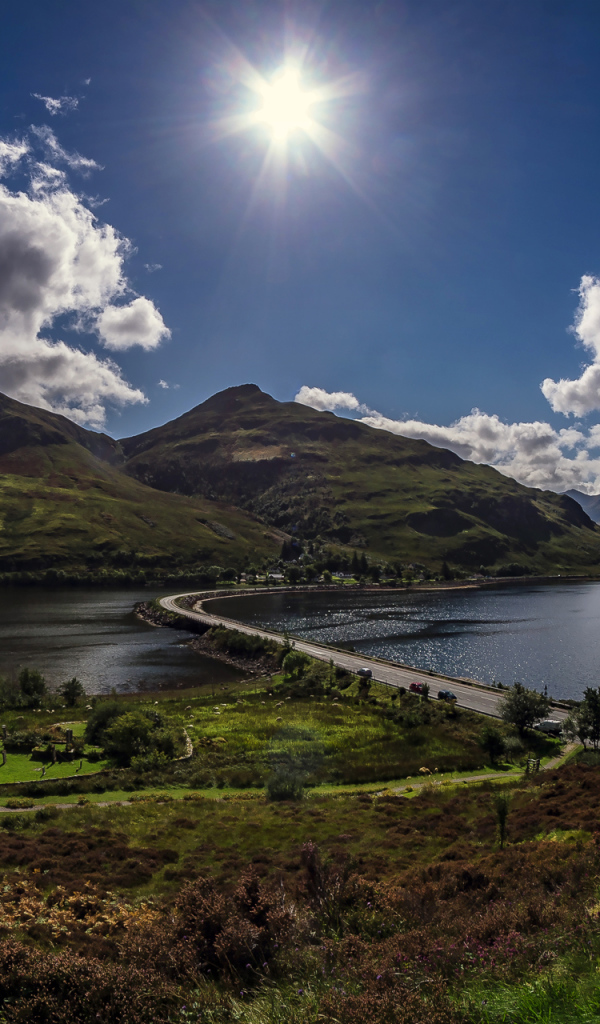 Яркое солнце в голубом небе над горами у реки