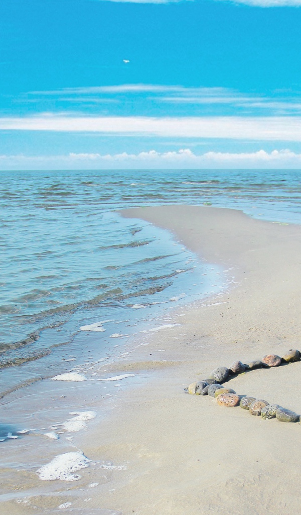 Сердце из камней на песке у спокойного моря под голубым небом