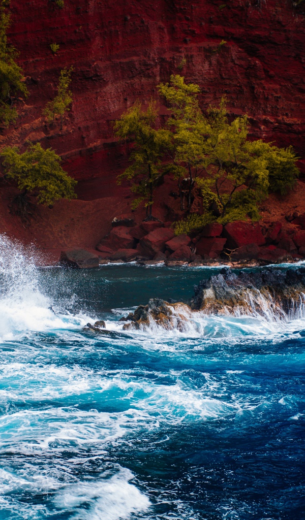 Грубое море брызгает камнями перед красным песчаным океанским заливом в Хане