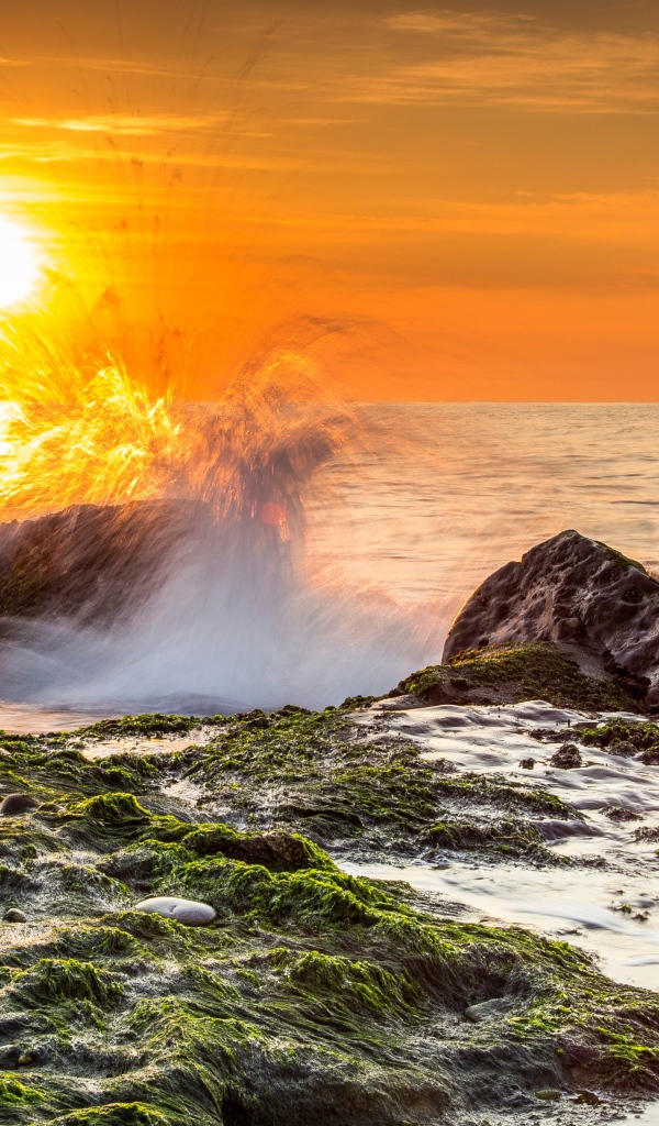 Бушующие волны в море бьются об камни на закате