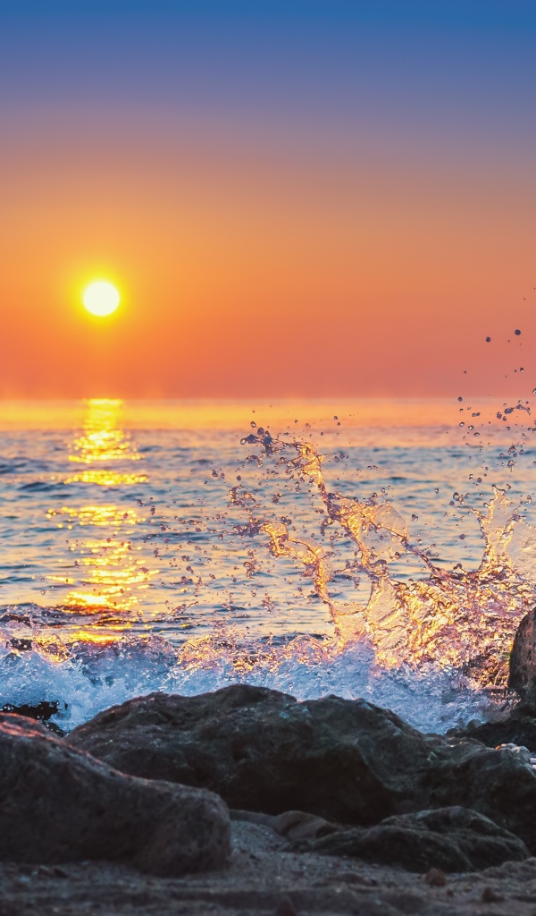 Волны бьются о камни на морском побережье на закате