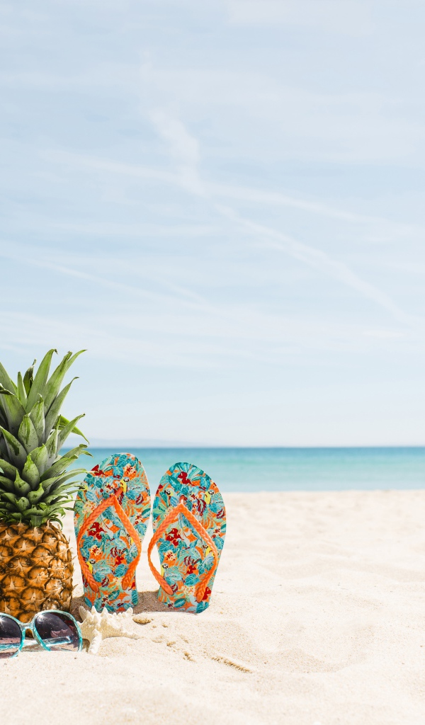 Сумка, ананас, шлепанцы и солнечные очки лежат на песке на пляже летом