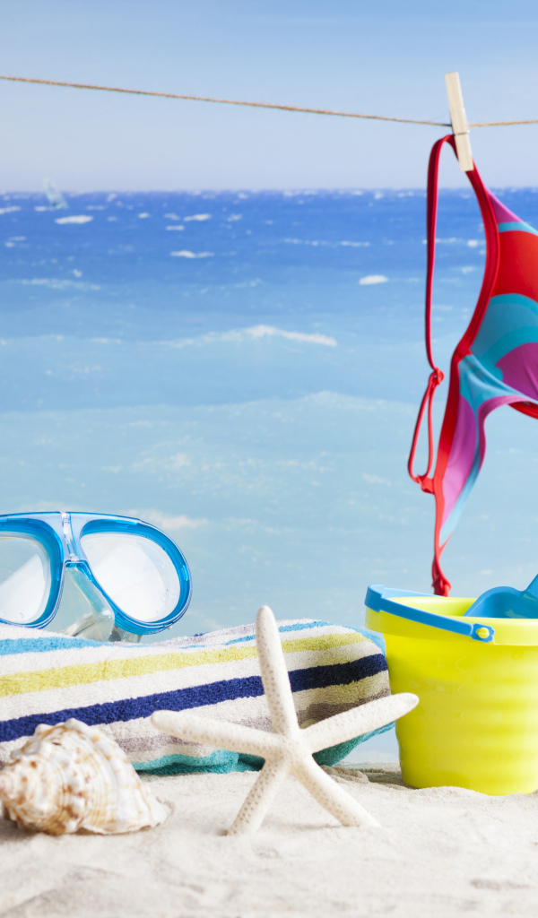 Очки, купальник, полотенце, ракушки и игрушки на песке на пляже летом