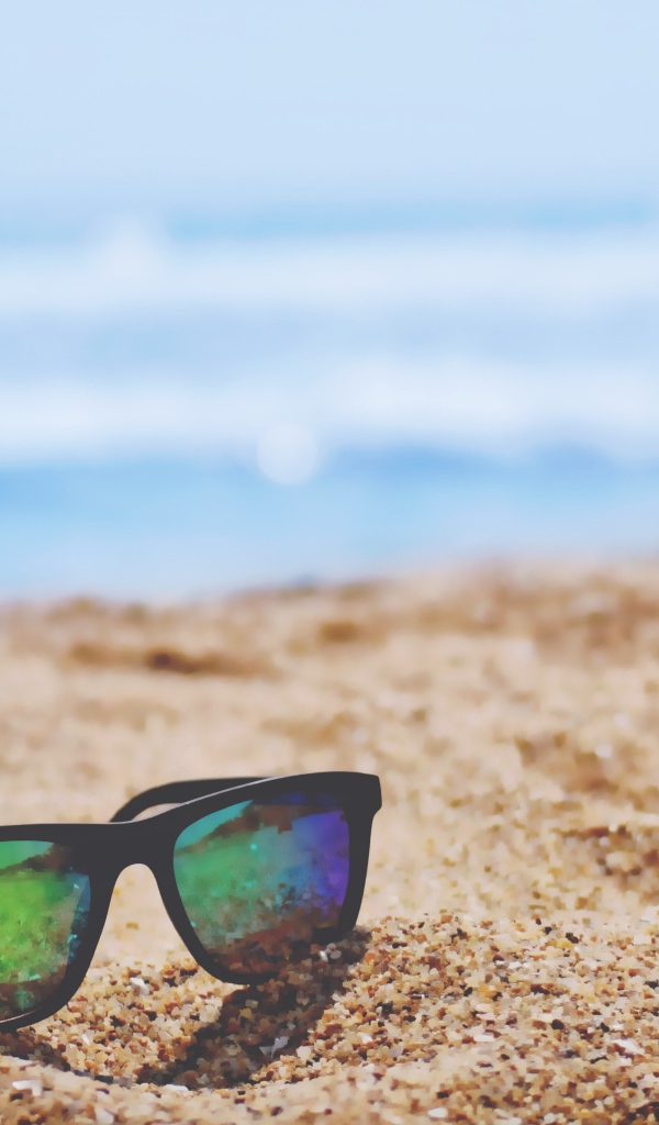 Солнцезащитные очки лежат на желтом песке у моря