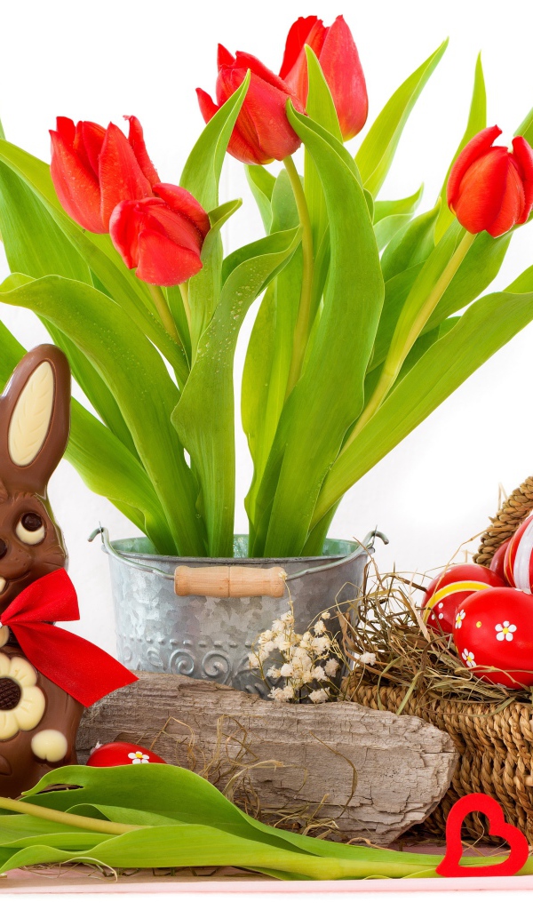 Букет красных тюльпанов на столе с шоколадным кроликом и крашеными яйцами на Пасху
