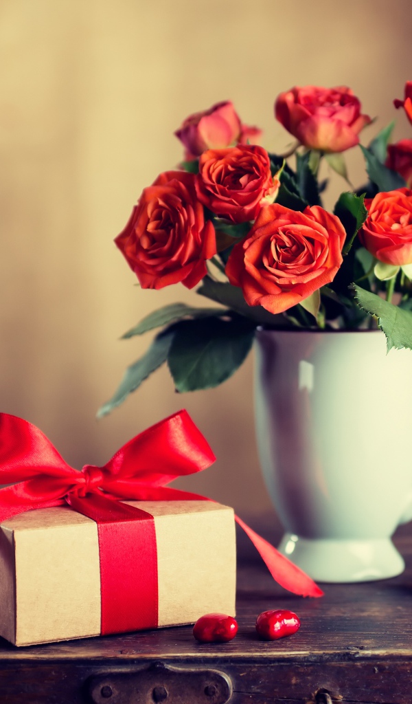 Букет роз в белой вазе с подарком на столе