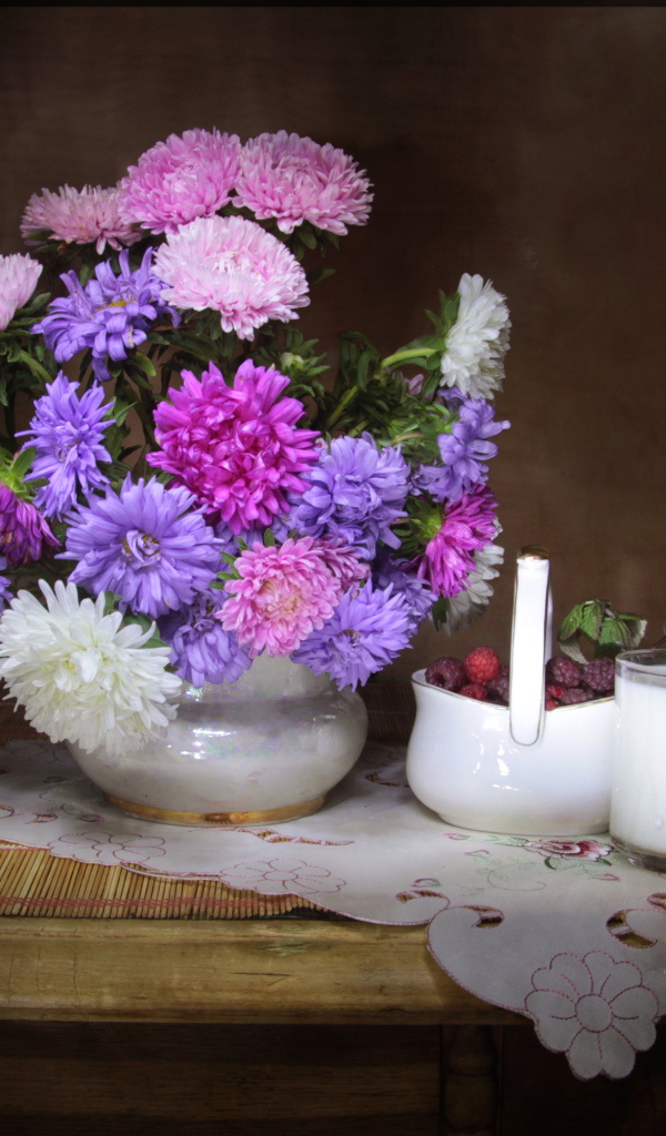 Букет разноцветных астр в вазе на столе с молоком и ягодами малины