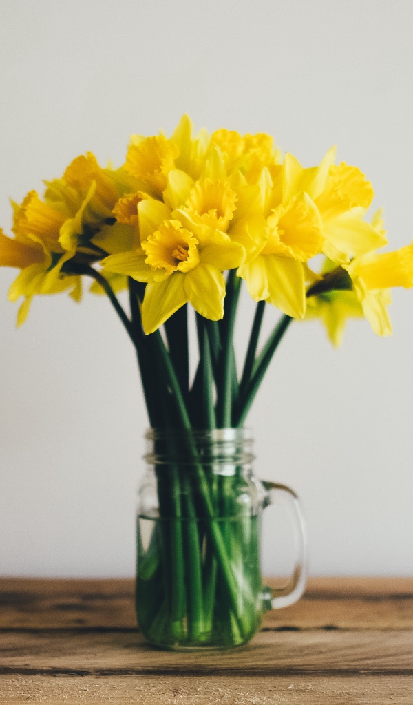 Букет желтых нарциссов в стеклянной вазе на столе 