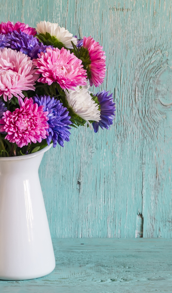 Разноцветные астры в вазе на деревянном фоне
