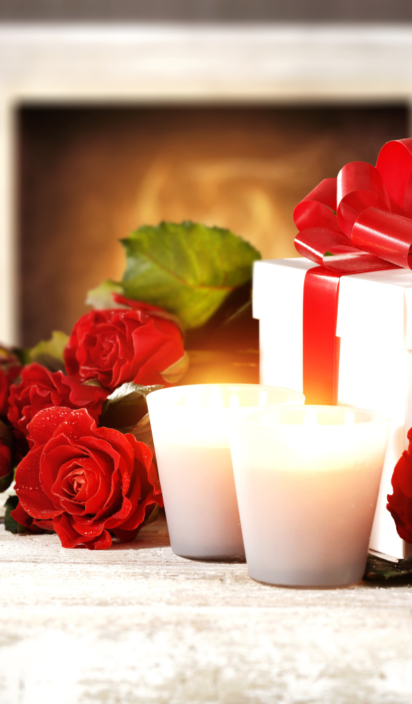 Красные розы с подарком и двумя зажженными свечами на столе
