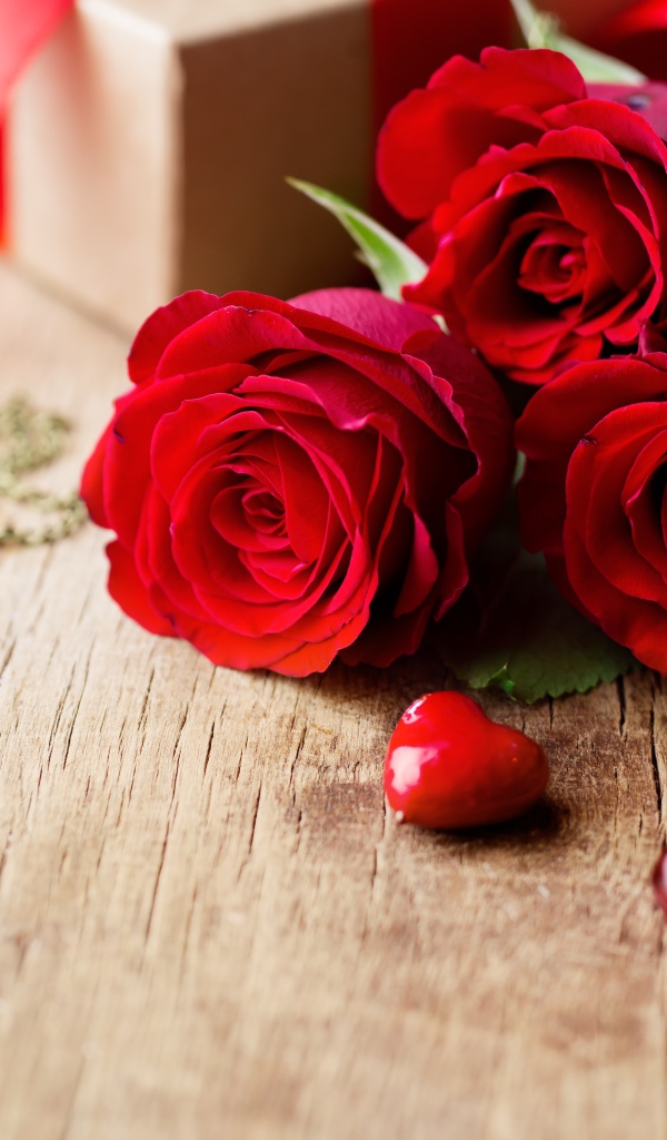 Три красных розы на деревянном столе с красными сердечками