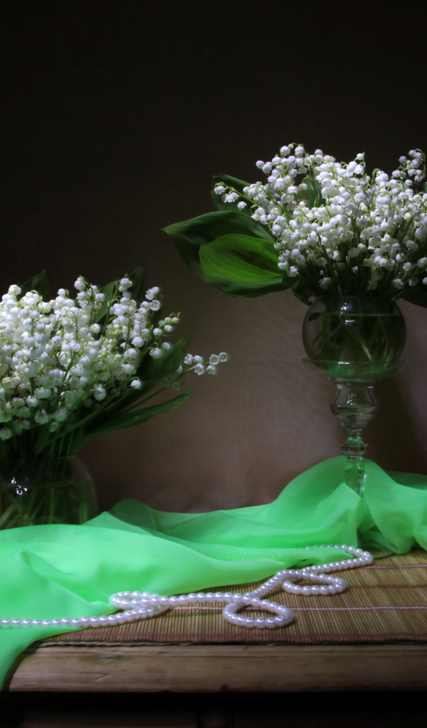Два букета ландышей с бусами на столе 