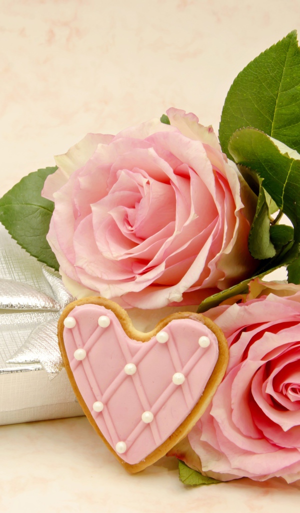 Две розовые розы с печеньем в виде сердца на розовом фоне