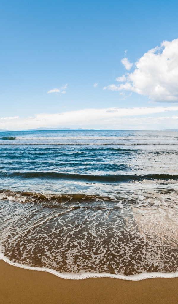 Морская волна на песке под красивым небом с белыми облаками
