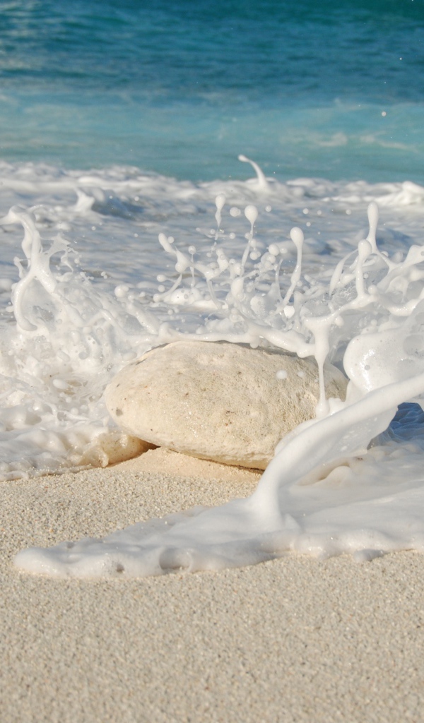 Белые морские волны бьются об камень на желтом песке