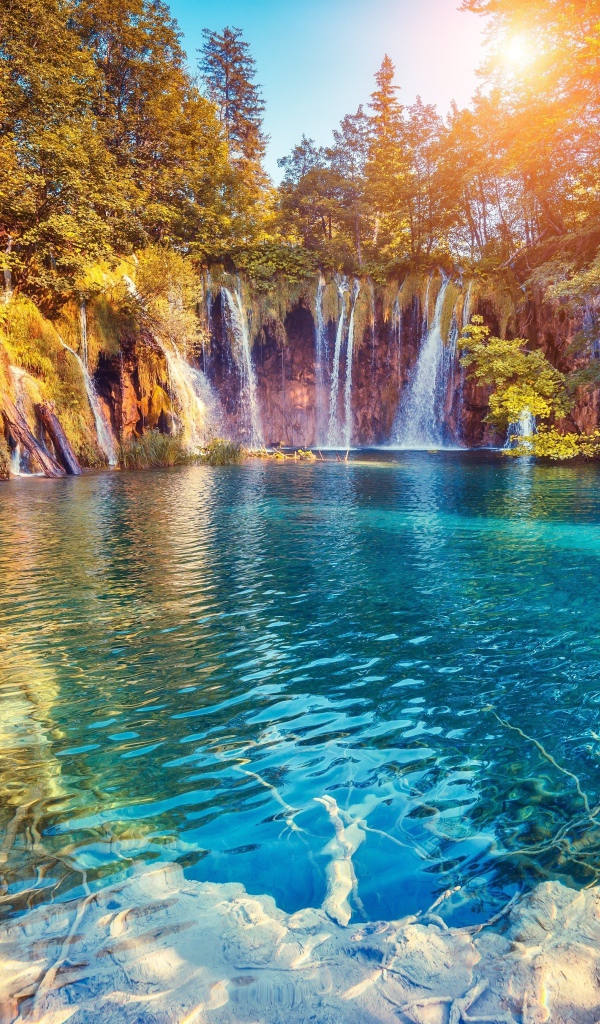 Водопад в лучах солнца стекает со скалы в реку