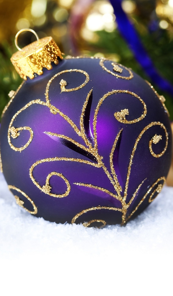 Красивая фиолетовая елочная игрушка лежит на снегу