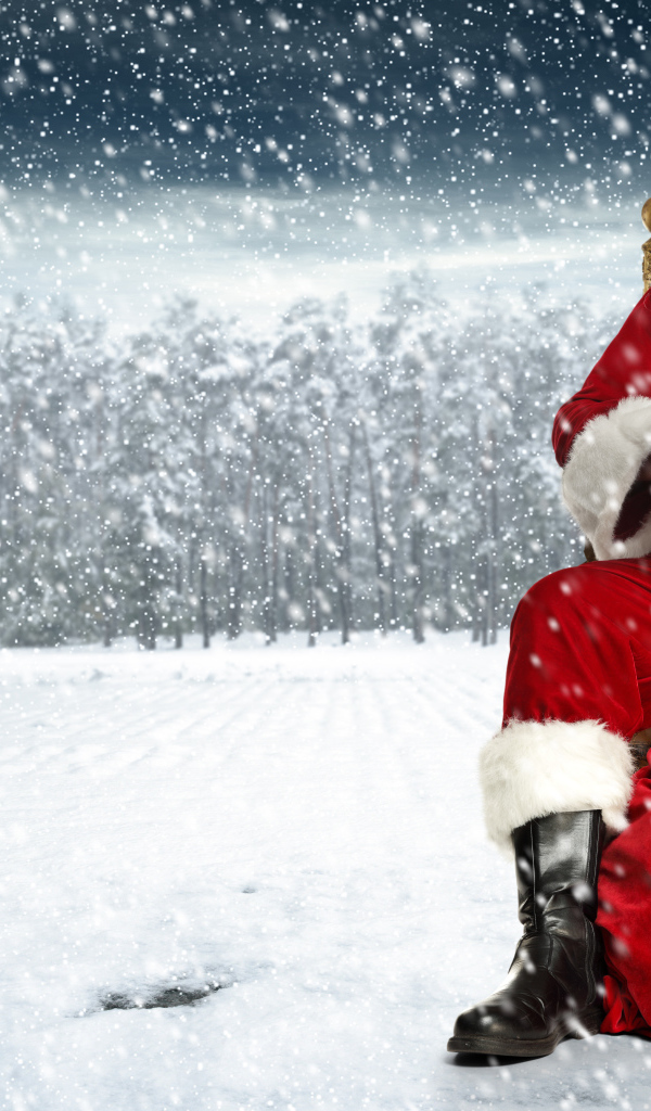 Веселый Санта Клаус сидит на мешке в заснеженном лесу