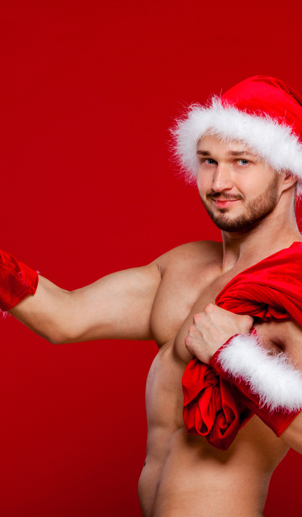 Мужчина в новогоднем костюме Санта Клауса с мешком и подарком в руке на красном фоне