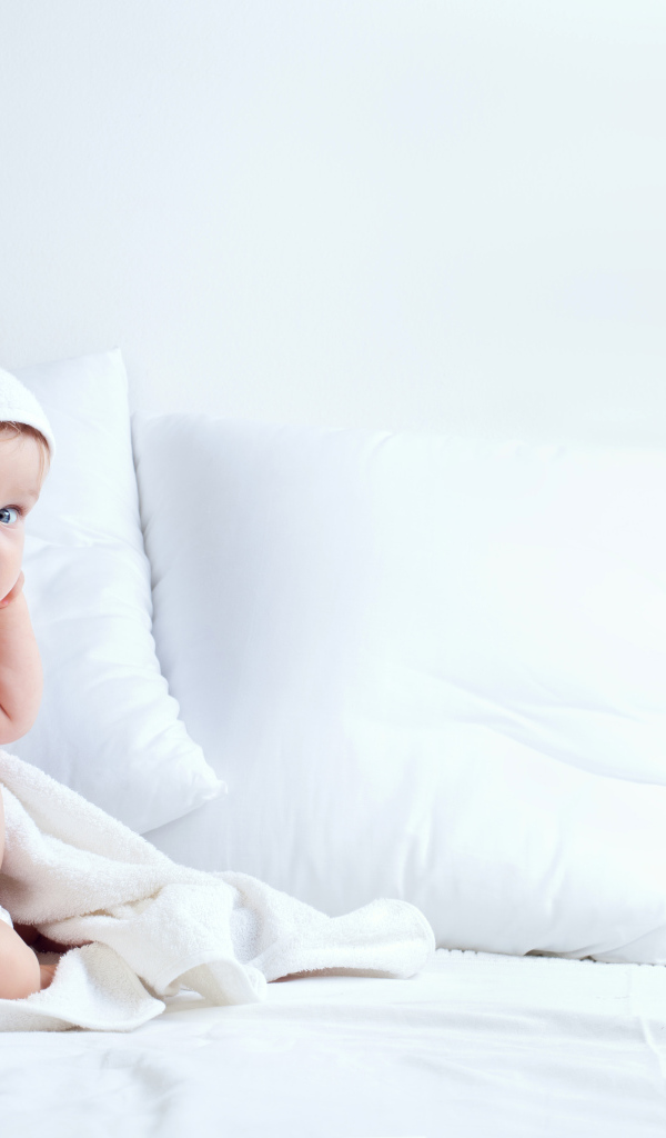 Грудной ребенок сидит на кровати с подушками