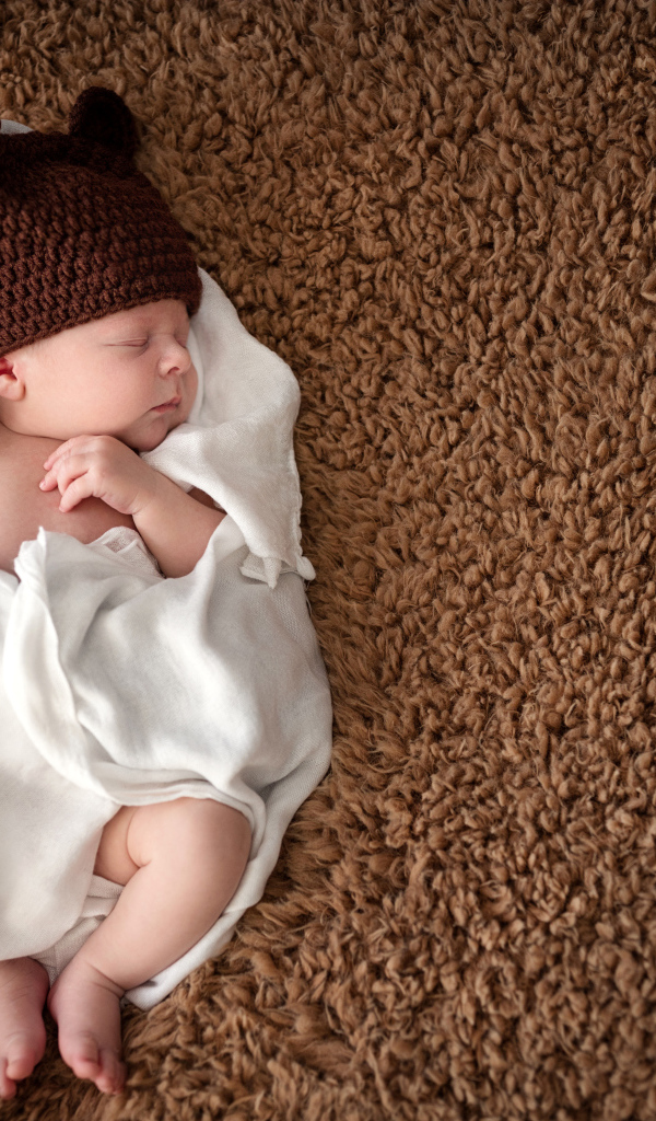 Грудной ребенок в вязаной шапке  спит в белом покрывале 
