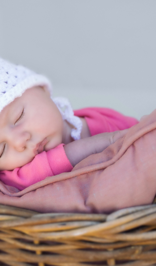 Маленький ребенок в белой шапке спит в корзине