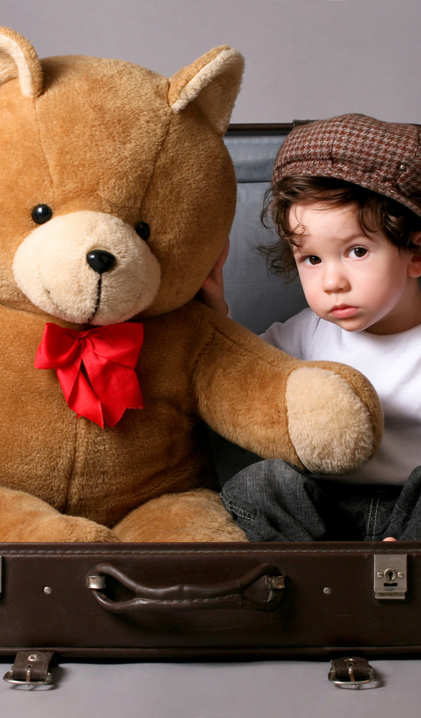Маленький мальчик сидит в чемодане с плюшевым мишкой 