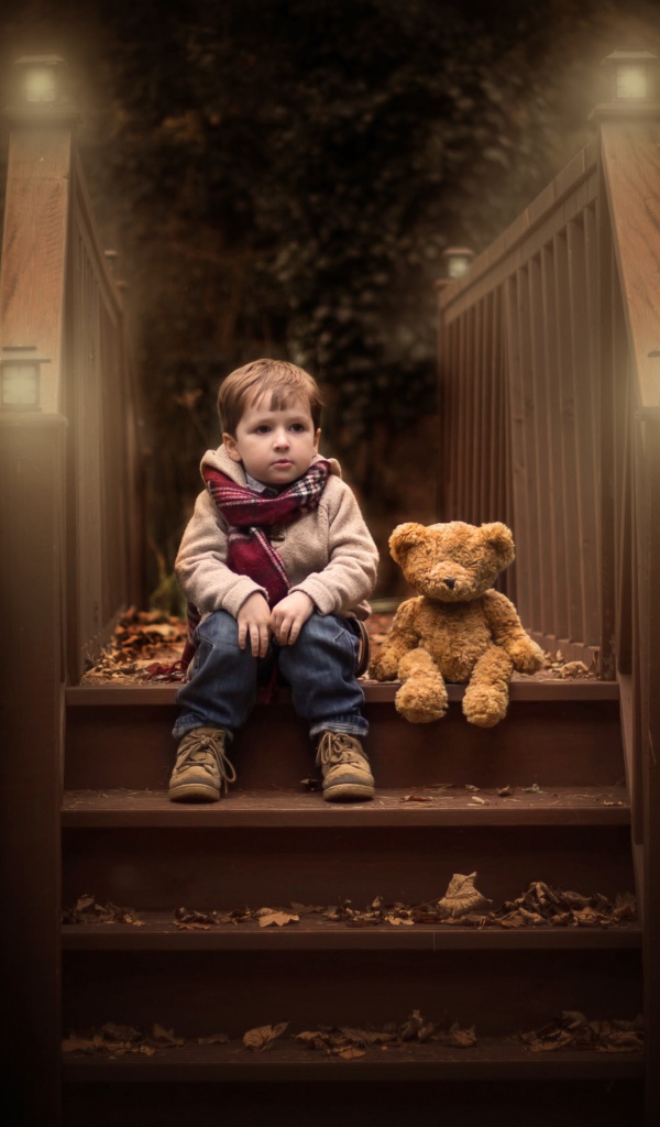 Маленький мальчик сидит с игрушечным мишкой на ступеньках