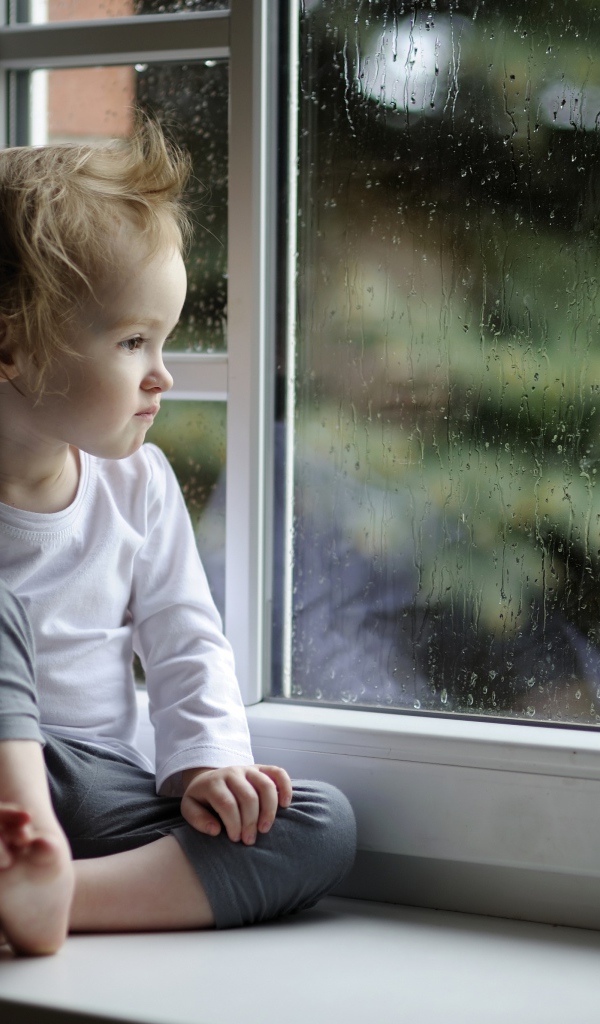 Маленькая девочка сидит на подоконнике у окна