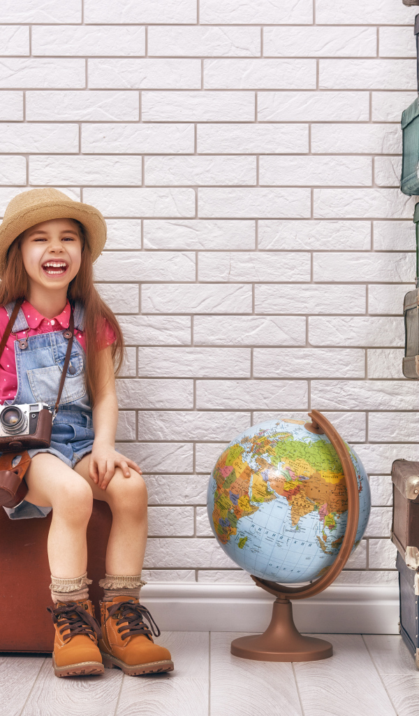 Маленькая девочка с фотоаппаратом сидит на чемодане