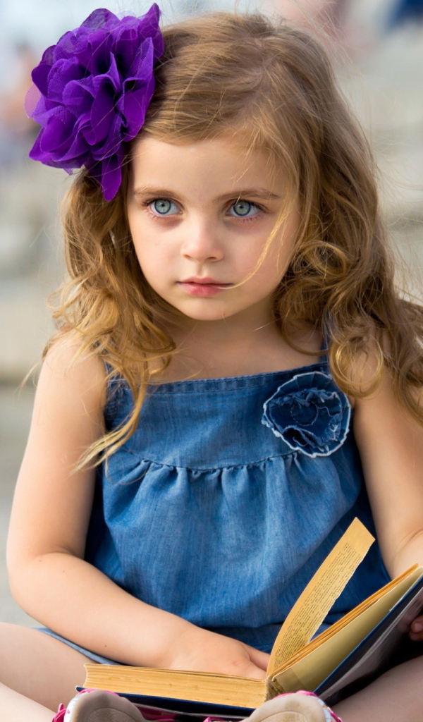 Маленькая девочка с цветком в волосах сидит на ступенях