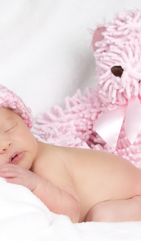 Спящий грудной ребенок в шапке с большим розовым медведем