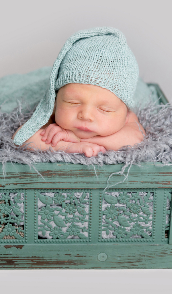 Спящий ребенок в зеленом ящике на сером фоне