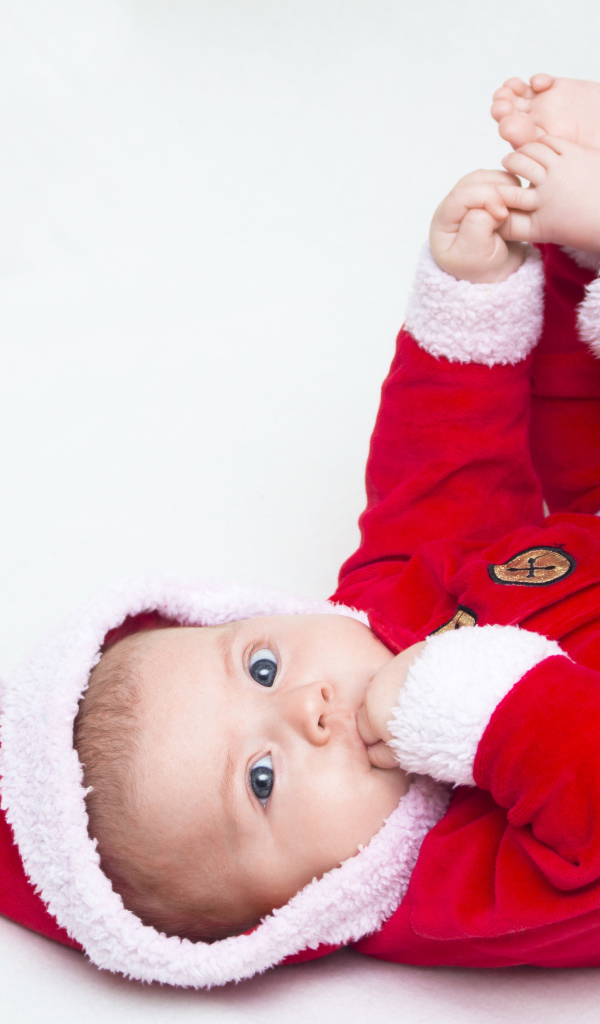 Маленький ребенок в красном новогоднем костюме на сером фоне