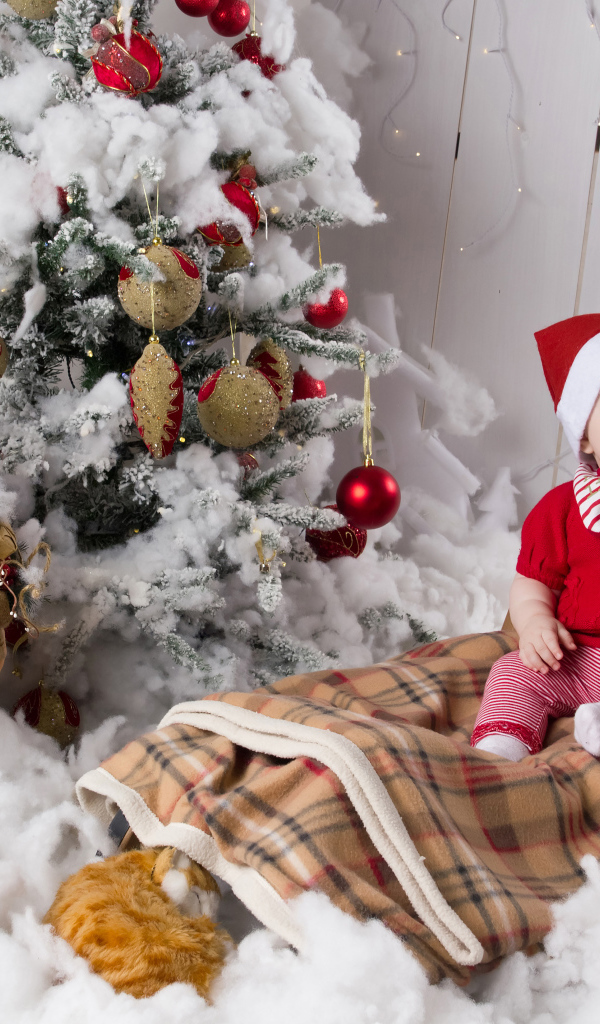 Маленький ребенок в санях у елки с дедом морозом на Новый год 