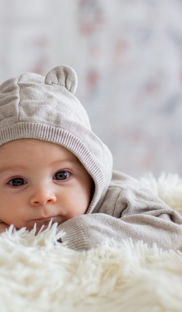 Маленький ребенок лежит на белом меховом покрывале 