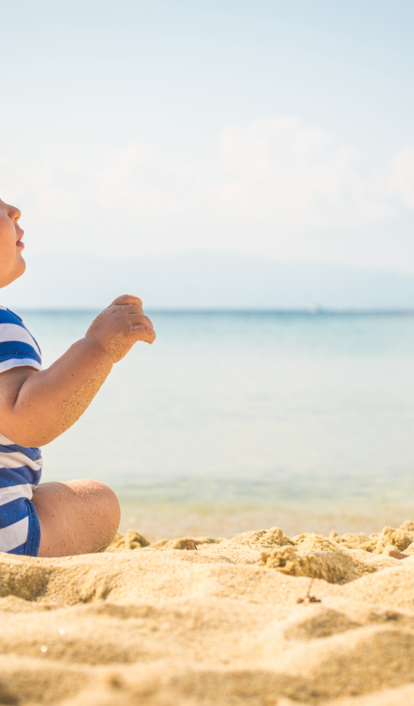 Маленький ребенок сидит на песке на пляже у моря