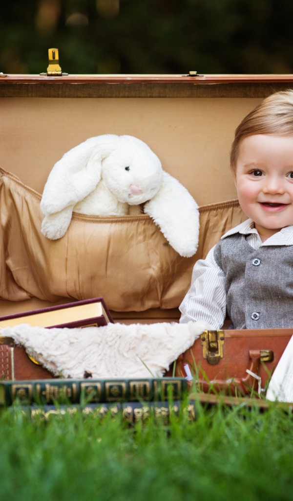 Улыбающийся мальчик сидит в чемодане с книгами