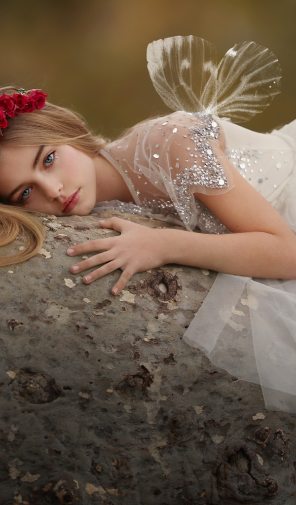 Красивая маленькая девочка в белом платье лежит на камне