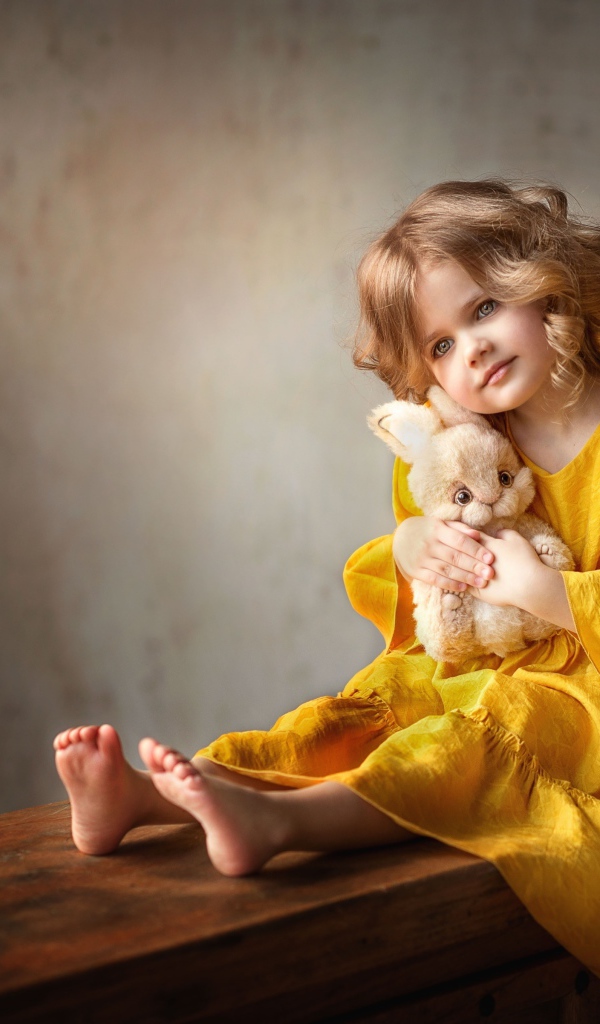 Beautiful little girl in yellow dress with toy