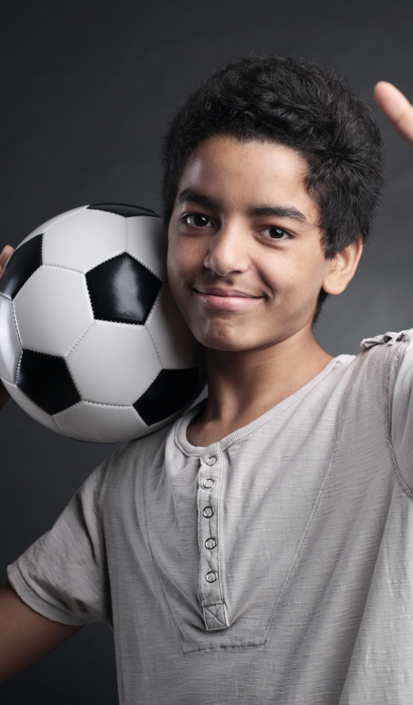 Мальчик с футбольным мячом на плече на сером фоне