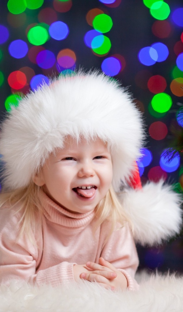 Смешная девочка в новогодней шапке у елки