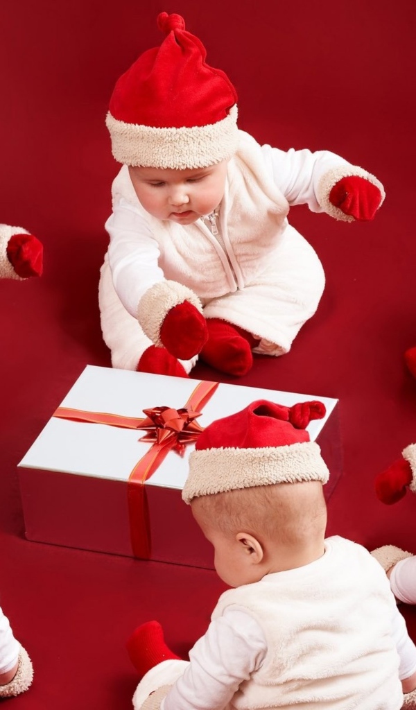 Младенцы в новогодних костюмах с подарком на красном фоне