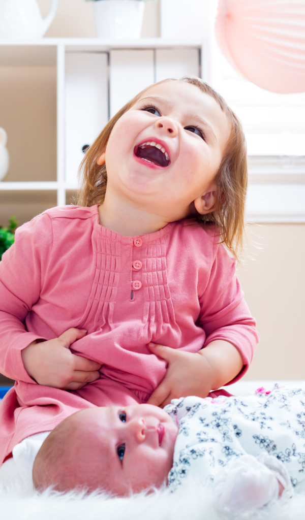 Смеющаяся маленькая девочка с младенцем