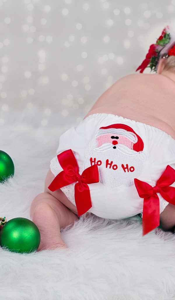 Маленькая грудная девочка с новогодними игрушками на белом покрывале 