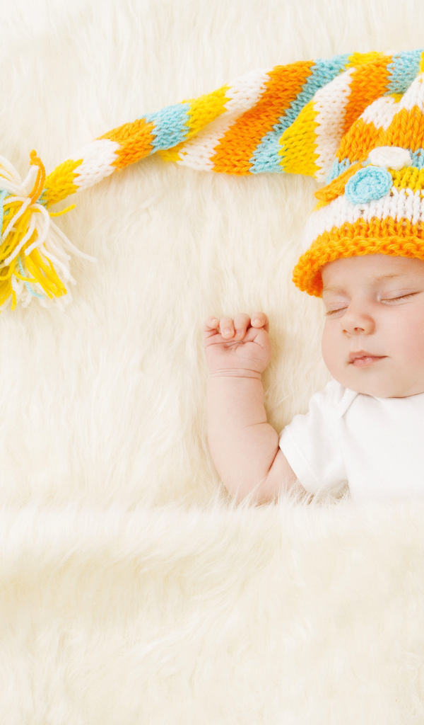 Маленький спящий под меховым покрывалом малыш в вязаной шапке