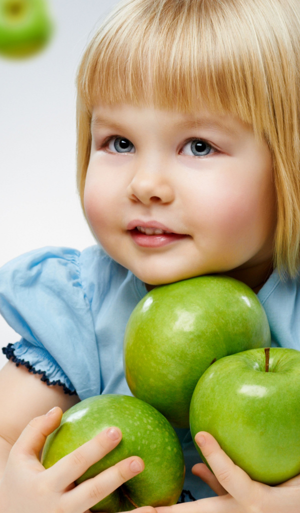 Маленькая девочка блондинка с зелеными яблоками