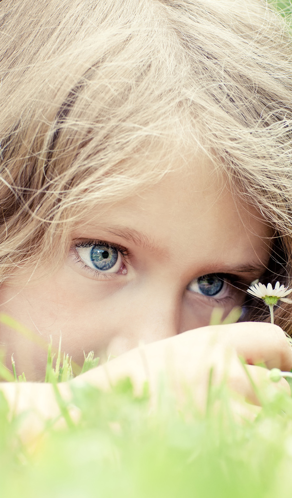 Маленькая голубоглазая девочка на траве с ромашкой